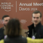 Unscharf abgebildete Personen vor einer braunen Wand mit dem Logo des Weltwirtschaftsgipfels Davos 2024.