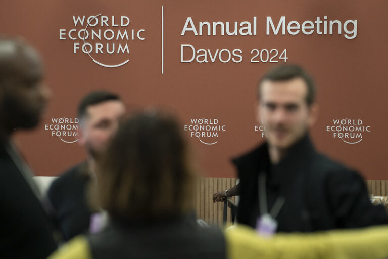 Unscharf abgebildete Personen vor einer braunen Wand mit dem Logo des Weltwirtschaftsgipfels Davos 2024.