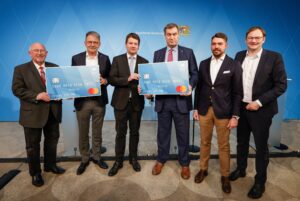 Das Bild zeigt unter anderem Bayerns Ministerpräsident Markus Söder und Innenstaatssekretär Sandro Krichner bei der Präsentation einer übergroßen Bezahlkarte für Asylbewerber.