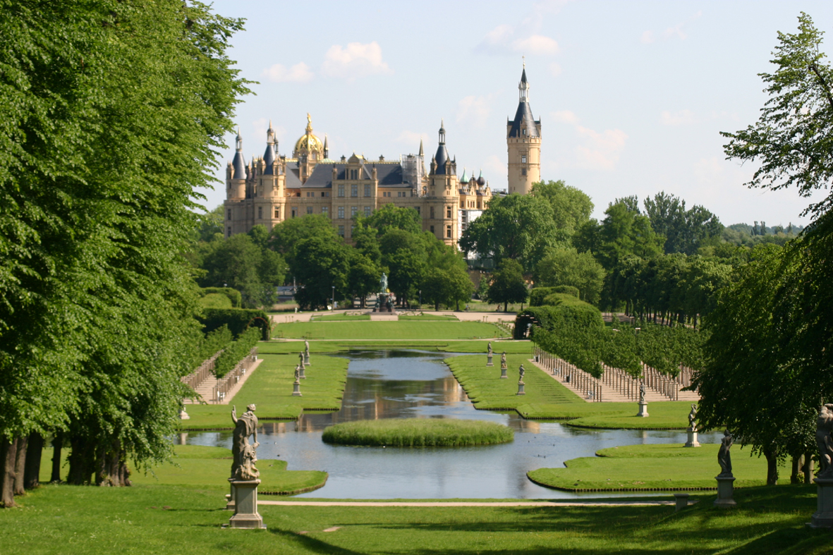 Blick auf das Schweriner Schloss, im Vordergrund eine barocke Gartenanlage mit Wasserbecken.