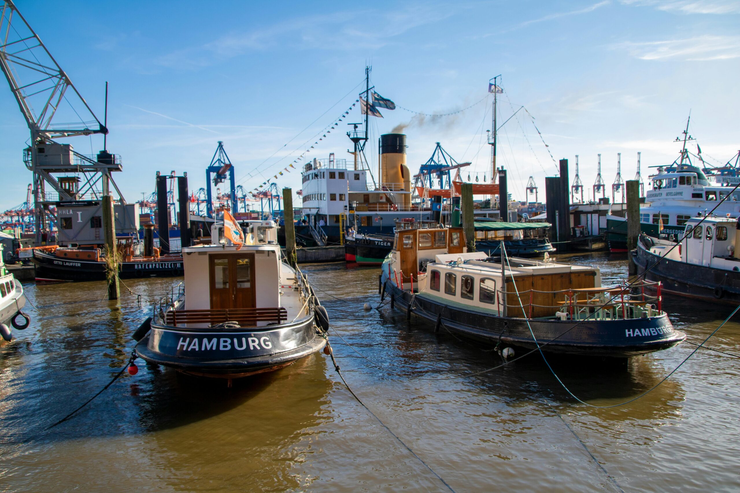 Blick in ein kleines Hafenbecken, im Vordergrund liegen mehrere kleinere Schiffe mit der Aufschrift "Hamburg".