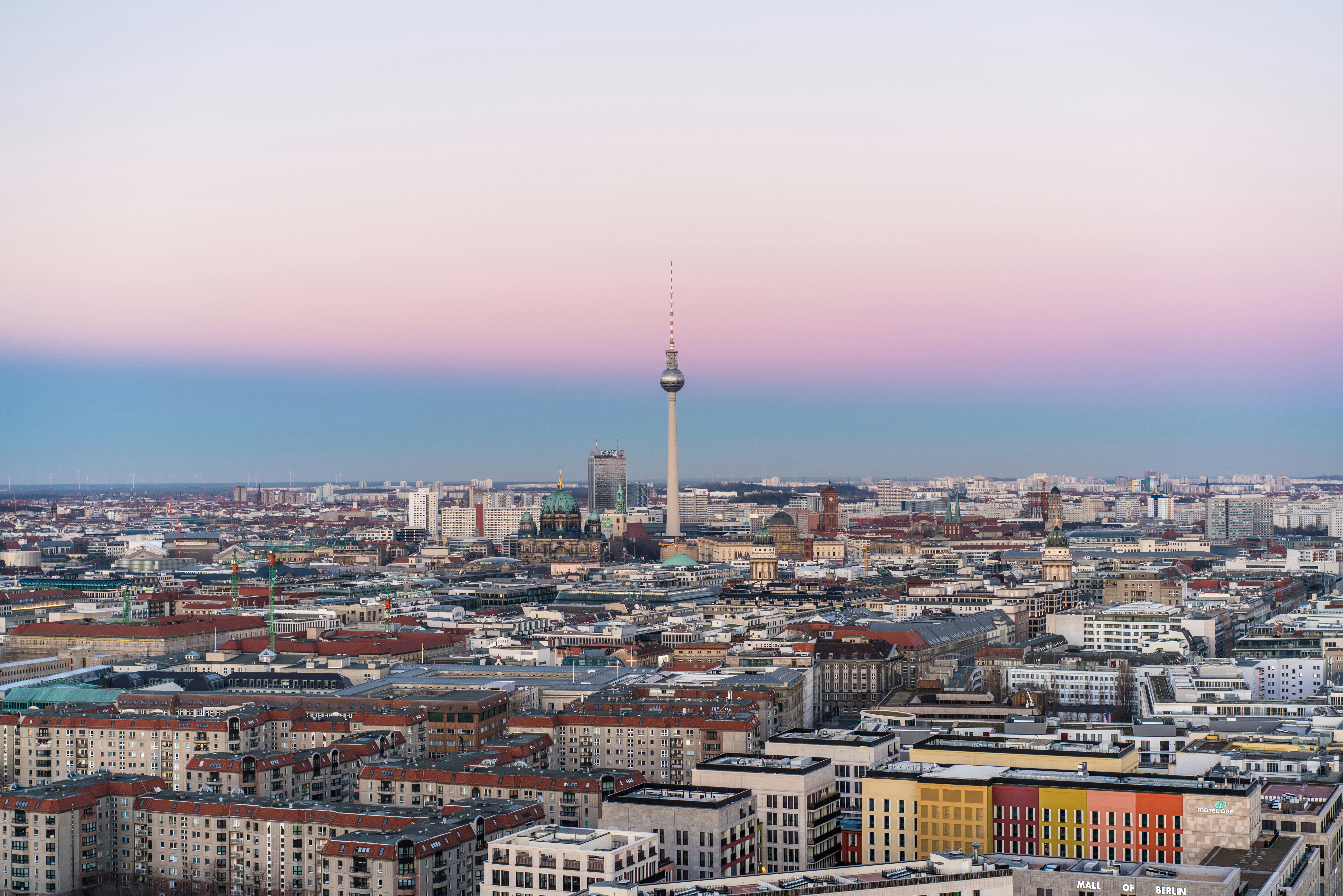 Luftbild-Panorama er Stadt berlin, im Mittelpunkt der Fernsehturm, im Hintergrund leicht dunstiger, blau-rosafarbener Himmel.