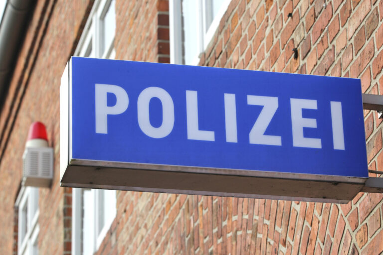 Blaues Schild mit weißer Aufschrift Polizei, an einer Ziegelwand montiert.