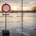 Blick auf eine überschwemmte Fläche, im Vordergrund ein Schild mit der Aufschrift "Hochwasser".