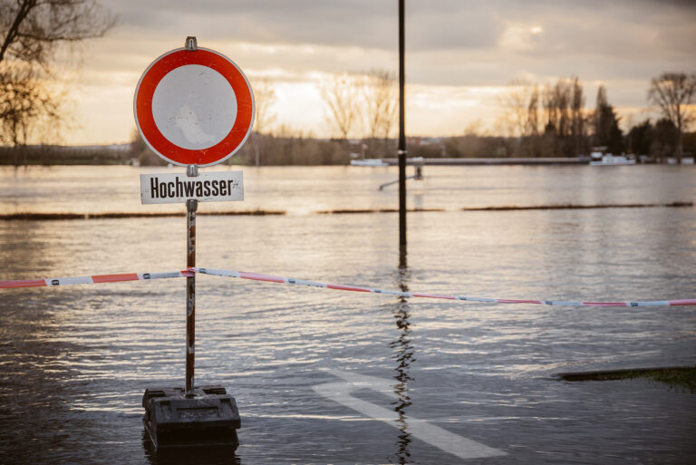 Blick auf eine überschwemmte Fläche, im Vordergrund ein Schild mit der Aufschrift "Hochwasser".