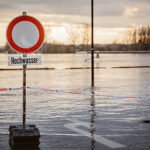 Hochwasserwarnschild vor einer überfluteten Fläche