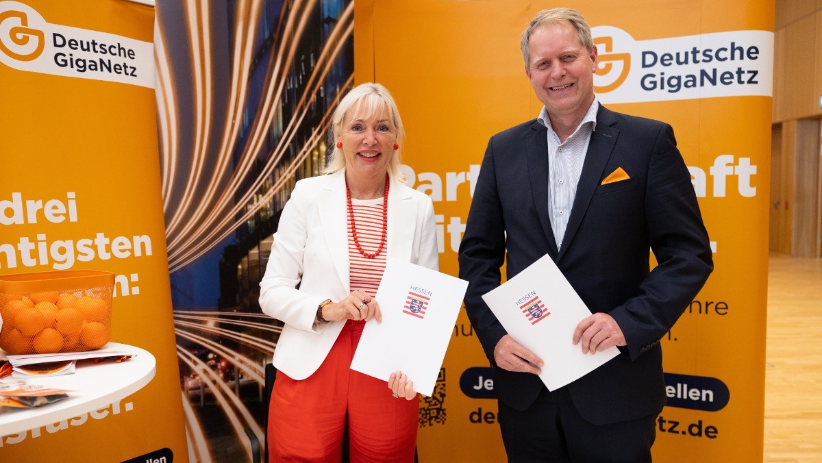 Hessens Digitalministerin Senemus und Jan Budden, Geschäftsführer der Deutschen GigaNetz, stehen mit Verträgen in der Hand nebeneinander.