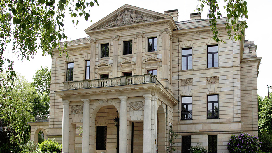 Blick auf die klassizistische Fassade einer Sandsteinvilla, umgeben von Bäumen (Sitz des BKG).