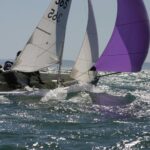 Glitzerndes Meer, darauf eine Jolle mit violettem Spinnaker.