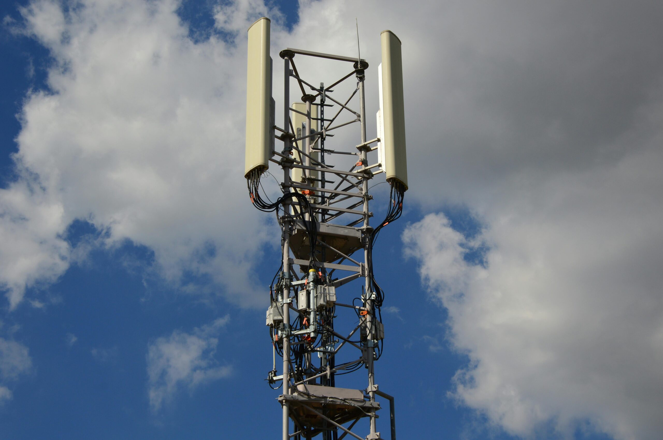 Blick aus der Untersicht auf einen Mobilfunkmasten, im Hintergrund blauer Himmel mit einigen Wolcken.