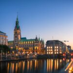 Ansicht der Innenstadt von Hamburg, im Vorergrund eine Wasserfläche, am Himmel Abenddämmerung.