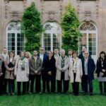 Personengruppe in förmlicher Kleidung steht auf einer Wiese vor einer historischen Sandsteinfassade.