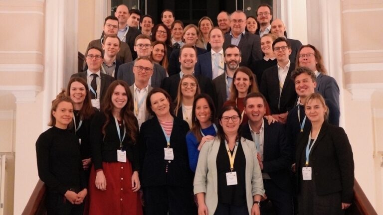 Gruppe von Personen in formeller Kleidung, auf einer Treppe zum Gruppenfoto aufgestellt.