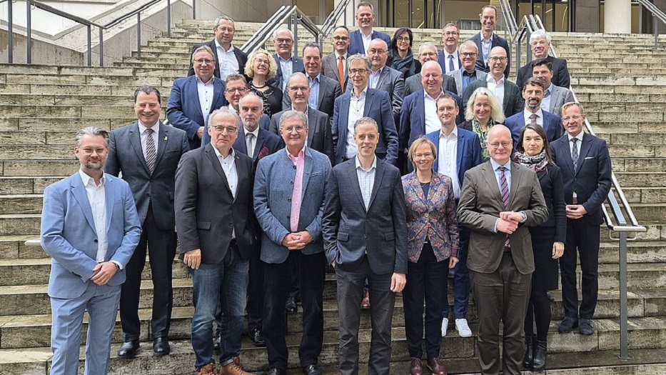 Gröere Gruppe von Personen in formaler Kleidung auf einer Treppe, alle blicken Richtung Kamera.