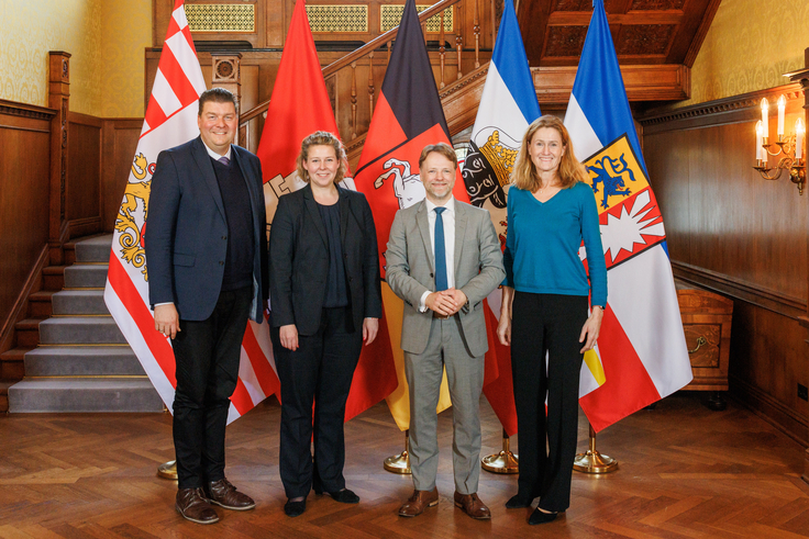 Die Finanzministerinnen und -Minister der Länder Hamurg, Bremen, Niedersachsen und Schleswig-Holstein stehen vor einer Treppe, im Hintergrund sind die jeweiligen Landesfahnen drapiert.