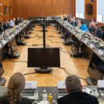 Treffen der Bundesinnenministerin mit Vertreterinnen und Vertretern der großen Social-Media-Plattformen und Digitalkonzerne: Blick in einen großen Sitzungssaal mit im Rechteck angeordneten Tischen, die gut besetzt sind.