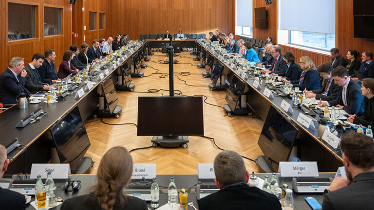 Treffen der Bundesinnenministerin mit Vertreterinnen und Vertretern der großen Social-Media-Plattformen und Digitalkonzerne: Blick in einen großen Sitzungssaal mit im Rechteck angeordneten Tischen, die gut besetzt sind.