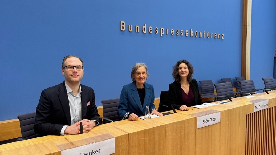 Ein Mann und zwei Frauen sitzen vor der blauen Wand der Bundespressekonferenz an einem langen Tisch mit Mikrofonen.