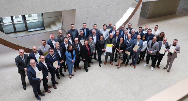 Modernes, großes Foyer mit hellgrauem Boden und Wänden, in dem eine größere Menschengruppe in formaler Kleidung zum Gruppenbild aufgestellt ist.