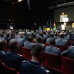 Ein Mann in Uniform hält vor einem großen Publikum an Soldatinnen und Soldaten eine Rede.